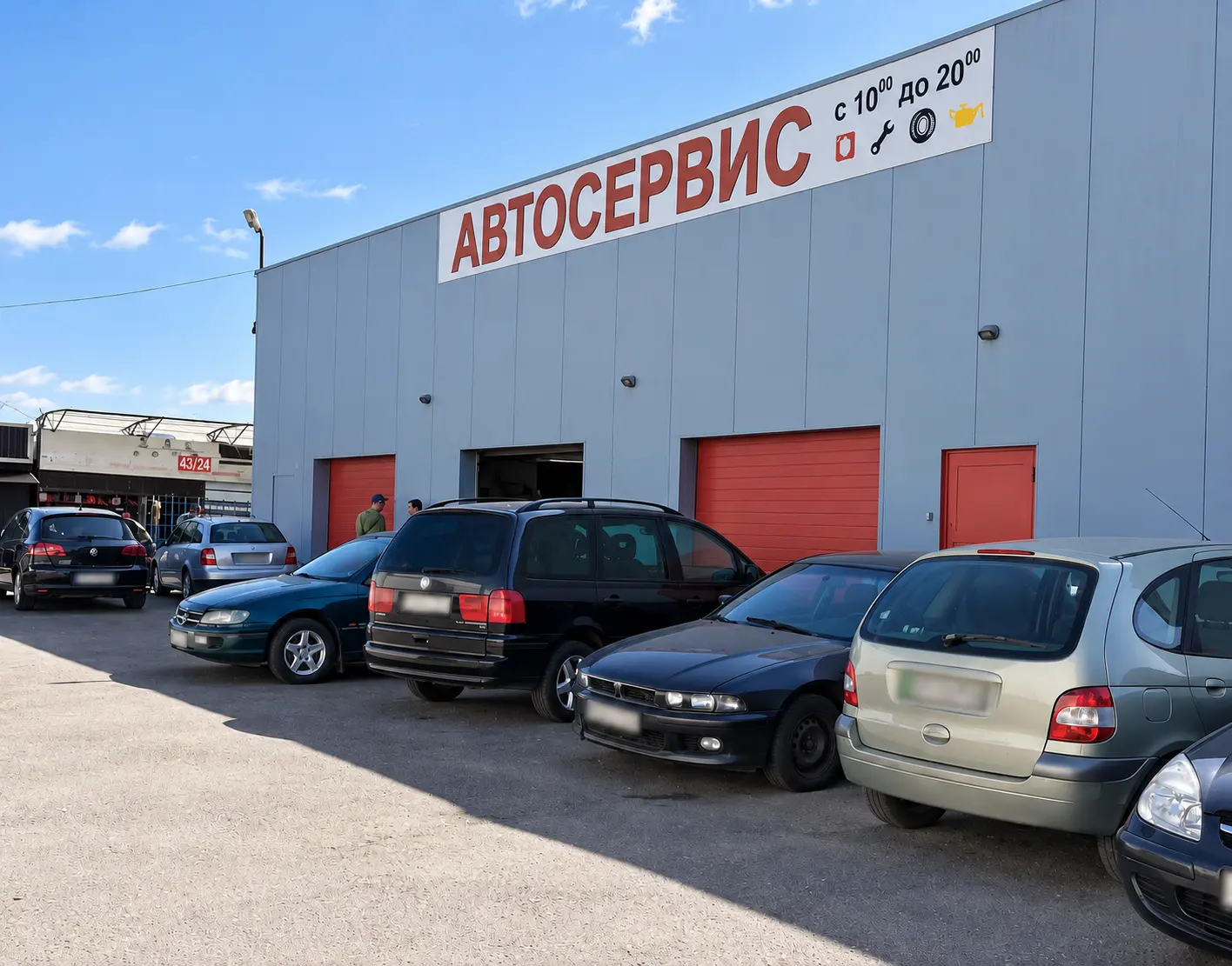 Фасад автосервиса: металлическое здание с большой вывеской «АВтосервис», красные ворота и парковка с машинами у входа
